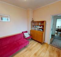 A room in a family house with a sofa, an armchair, and a display cabinet, with a wooden decor floor.
