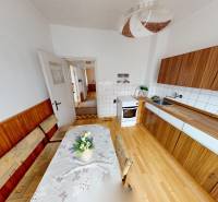 A kitchen in a family house with a wooden decor floor, a wooden bench, and a patterned tablecloth.