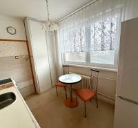 A kitchen in a 3-room apartment with a dining table, chairs, and a refrigerator.