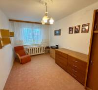 A room in a 3-room apartment with a carpet, a chest of drawers, an armchair, and wall shelves.