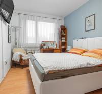 A bedroom with a bed, chair, and table in a 4-room apartment with a wood-patterned floor.