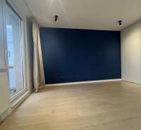 A room in a 3-room apartment with a blue wall, a floor with a wood decor, and balcony doors.