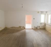 A room in a family house with a wooden decor floor and damaged walls.