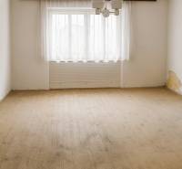 An empty room in a family house with a wood-decor floor and a large window with a curtain.