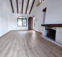 A room in a family house with a wooden decor floor, a fireplace, and wooden ceiling beams.