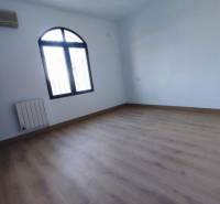 An empty room with an arched window, wood-patterned flooring, air conditioning, radiator.