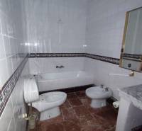 A bathroom in a family house with a bathtub, bidet, and a marble-patterned floor.
