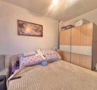 Bedroom in a family house with a painting above the bed, a large wardrobe, and a simple chair.