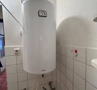 An electric boiler in the bathroom of a family house, covered with white ceramic tiles.