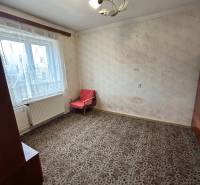 A room in a family house with a carpeted floor, a simple armchair, and curtains.