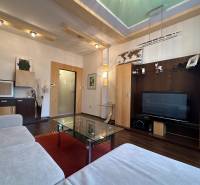 Living room in a two-room apartment with a sofa, glass table, and television, floor with wood decor.