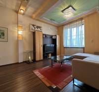 Living room of a two-room apartment with a sofa, television, wood-patterned flooring, and lighting fixtures.