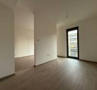 A room in a 2-room apartment with a wooden decor floor and balcony doors.