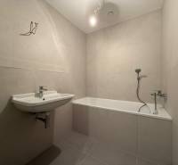 Bathroom in a 2-room apartment, light tiles, bathtub, sink, simple furnishings.