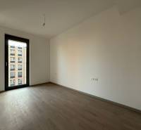 An empty room with wood-patterned flooring in a two-room apartment, large window with a view.