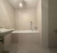 A bathroom in a 2-room apartment with a bathtub, sink, and neutral tiles.
