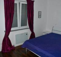Bedroom with purple curtains, a blue bedspread, and a wood-patterned floor in a family house.