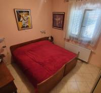 Bedroom in a family house with a double bed, colorful paintings, and light tiles.