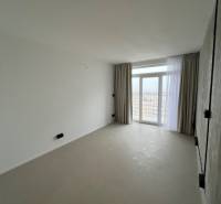Studio apartment with large windows, light curtains, and light flooring with a view of the city.