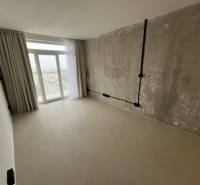 Bright studio apartment with exposed concrete, curtains, and balcony doors.