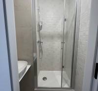 A shower corner with a sink in a studio apartment, with light tiles.