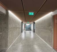 A long corridor with concrete walls and lighting leads to an escape route.