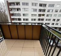 The balcony of a one-room apartment in Senica with a view of a panel building and a parking lot.