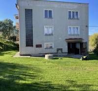 A family house in Hajnáčka with a lawn, trees, and garden tools in the yard.