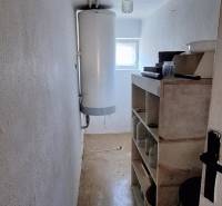 A narrow interior of a family house with a boiler and shelves, light walls, and a floor with a wooden decor.