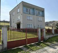 A family house in Hajnáčka with three floors, a red gate and fencing in front of it.