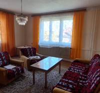 A living room in a family house with orange curtains, a sofa, and a coffee table.