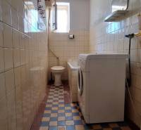 A narrow bathroom in a family house with a toilet, tiles, and a washing machine.