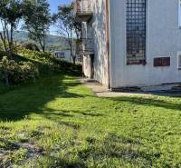 A family house in Hajnáčka with a grassy plot, trees, and balconies on a sunny day.