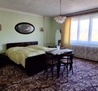 Bedroom in a family house with carpets, a bed, and a large window with curtains.