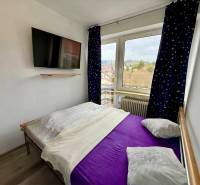 A bedroom in a family house with a television and a view through the window, floor with wooden decor.