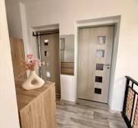 A hallway in a family house with light doors, a floor with a wood decor, and a decorative vase.