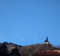 A tower in Banská Štiavnica with a blue sky and surrounded by trees.