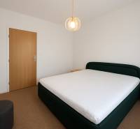 Bedroom in a 3-room apartment with a bed and a chair, white wall and wooden door.