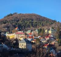 A view of Banská Štiavnica with forested hills and colorful buildings scattered across the slope.