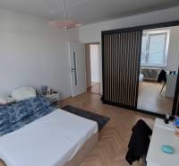 A bedroom in a three-room apartment with a wood-patterned floor and a built-in wardrobe.