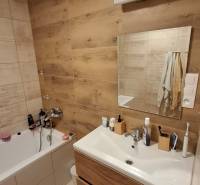 A bathroom with wooden floor decor, a bathtub, and a sink in a 3-room apartment.