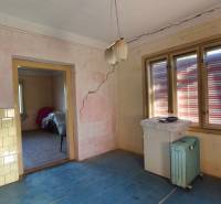 The interior of a family house with cracked walls, a blue floor, and an old radiator.