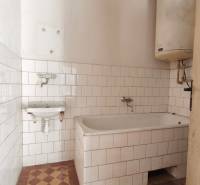 A bathroom in a family house with a bathtub, white tiles, and a water heater.