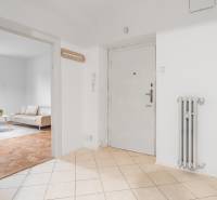 A hallway in a 3-room apartment with an entrance door, a radiator, and a view of the living room.
