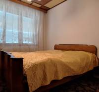 A bedroom with a bed, wardrobe, carpet, and a window with a lace curtain in a family house.