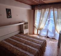 Bedroom in a family house with a bed, integrated shelf, and curtains over the windows.