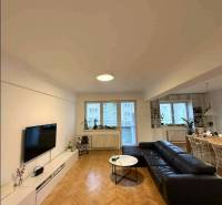 Living room in a 4-room apartment with a wood-patterned floor, black sofa, and TV.