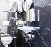 A bathroom with black marble tiles, a sink, a toilet, and soap dispensers in commercial premises.