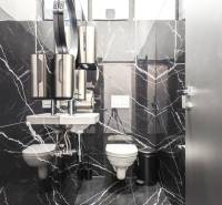 A restroom with black marble tiles, stainless steel accessories, and a sink in commercial premises.