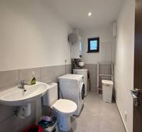 Bathroom in a family house with a washing machine, sink, and toilet, tiled floor.